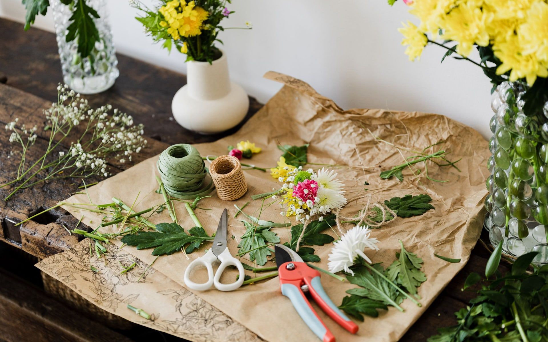 Packpapier mit Schere, Gartenschere, Schnur und geschnittenen Blumen auf einer Werkbank, von oben